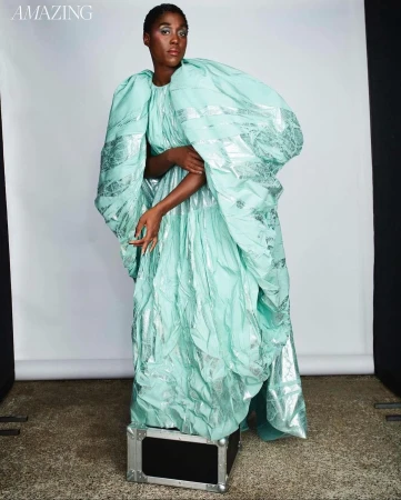 Black woman standing on a black case wearing a voluminous mint green dress with silver accents and dramatic puffy sleeves