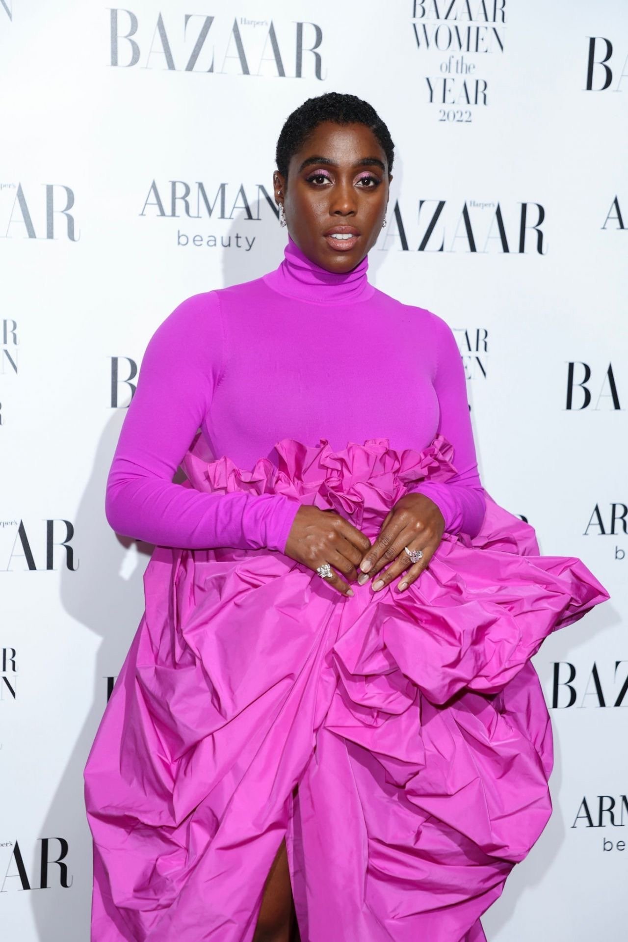 Black woman in a purple gown posing on a backdrop at the Bazaar Women of the Year event in a photo studio with soft lighting.