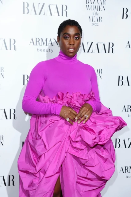 Black woman in a purple gown posing on a backdrop at the Bazaar Women of the Year event in a photo studio with soft lighting.
