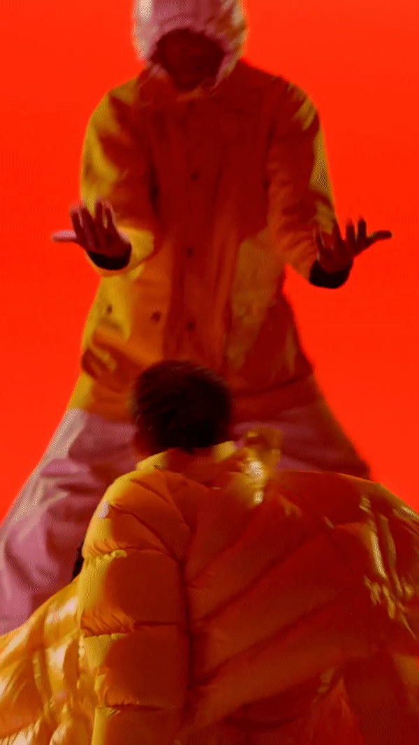 Two people in yellow puffy coats are set against a bright orange backdrop, creating a vibrant and eye-catching vertical studio shot.