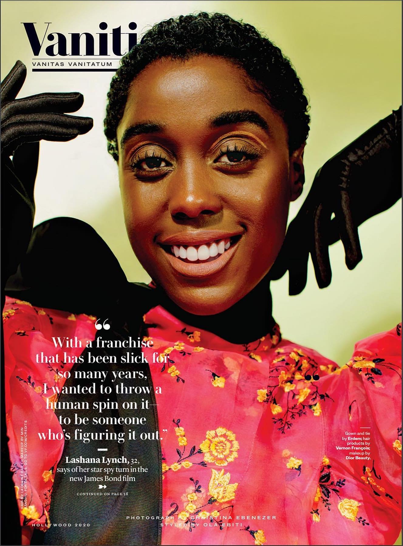 Close-up portrait of Lashana Lynch on the cover of Vanity Fair, wearing a floral top and black gloves, smiling at the camera.