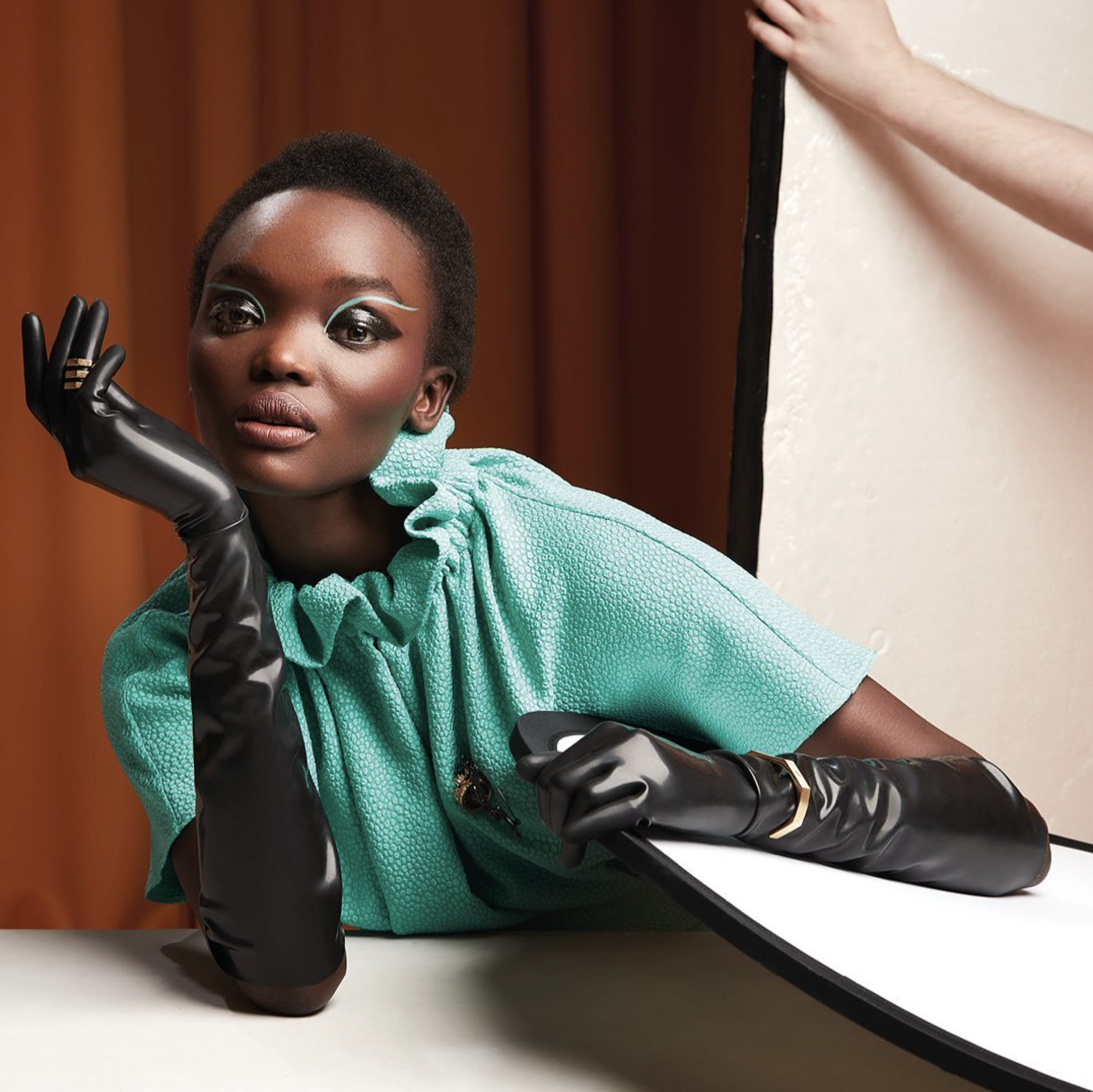 Portrait of a woman with an African appearance, wearing a green dress and long black gloves, posing with her hand against her face.