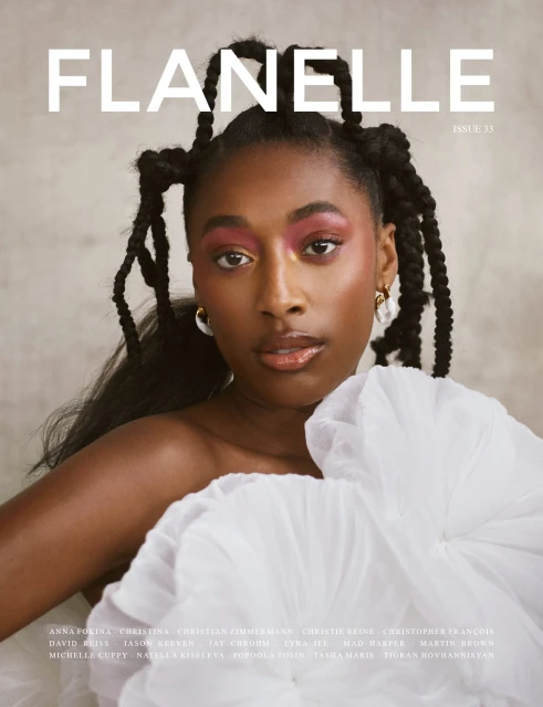 Magazine cover featuring a Black woman with elaborate braided hair, wearing pink eye shadow and a white ruffled top against a grey background.