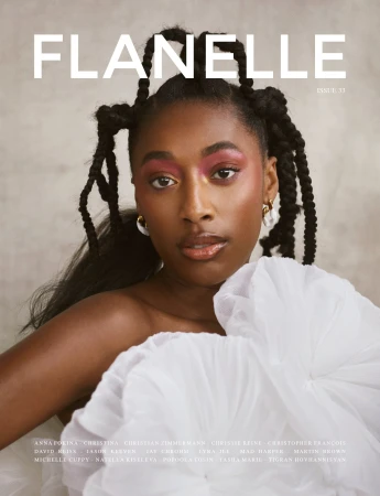 Magazine cover featuring a Black woman with elaborate braided hair, wearing pink eye shadow and a white ruffled top against a grey background.