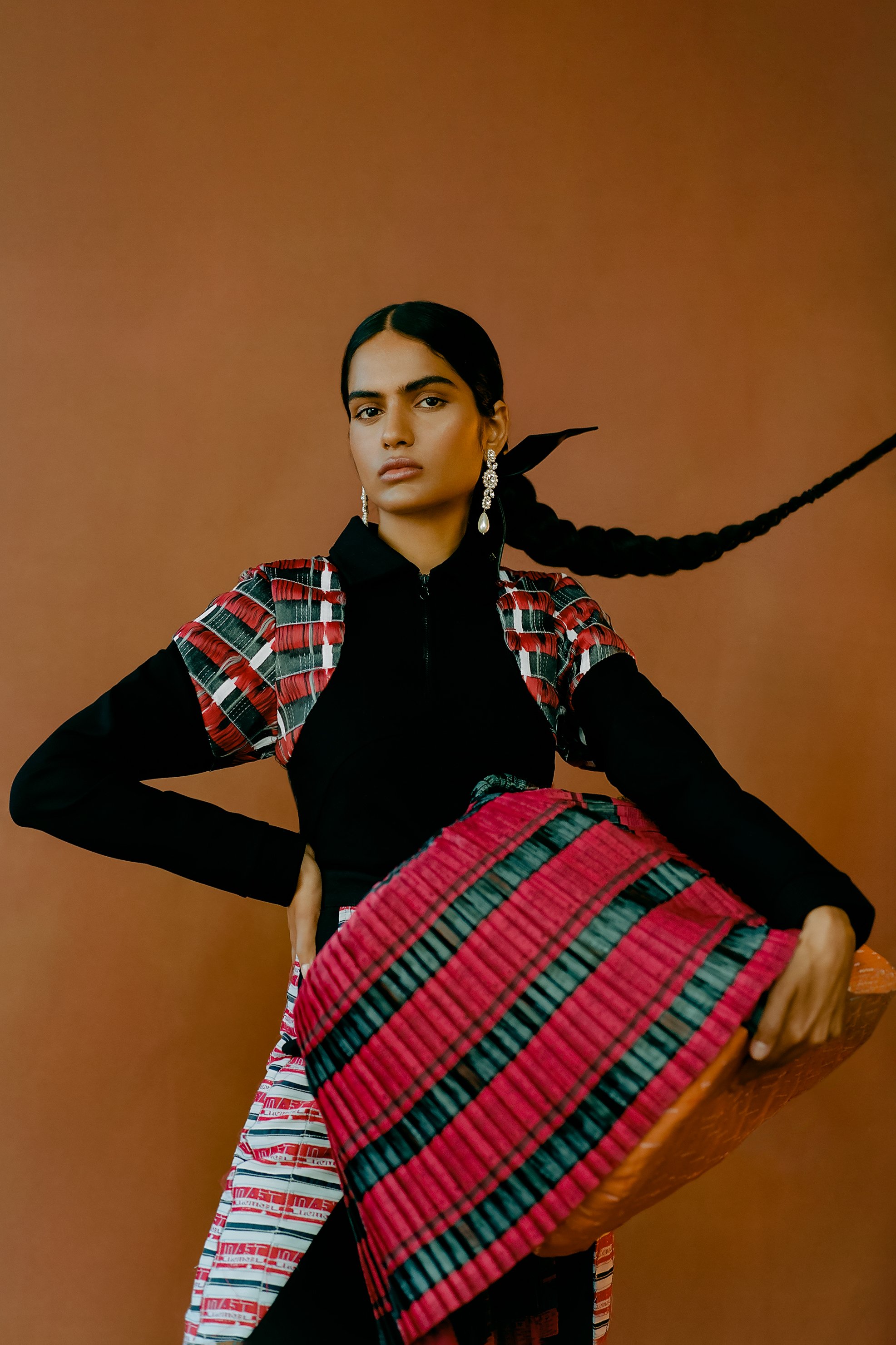 Portrait of a woman wearing a black turtleneck and a red plaid top holding a woven red and black patterned basket in front of a brown background.