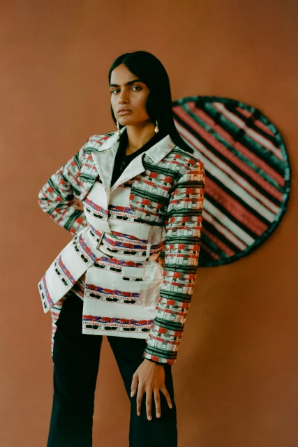A dark-haired adult female in a patterned jacket poses indoors with a geometric backdrop. Fashion and portrait photography.