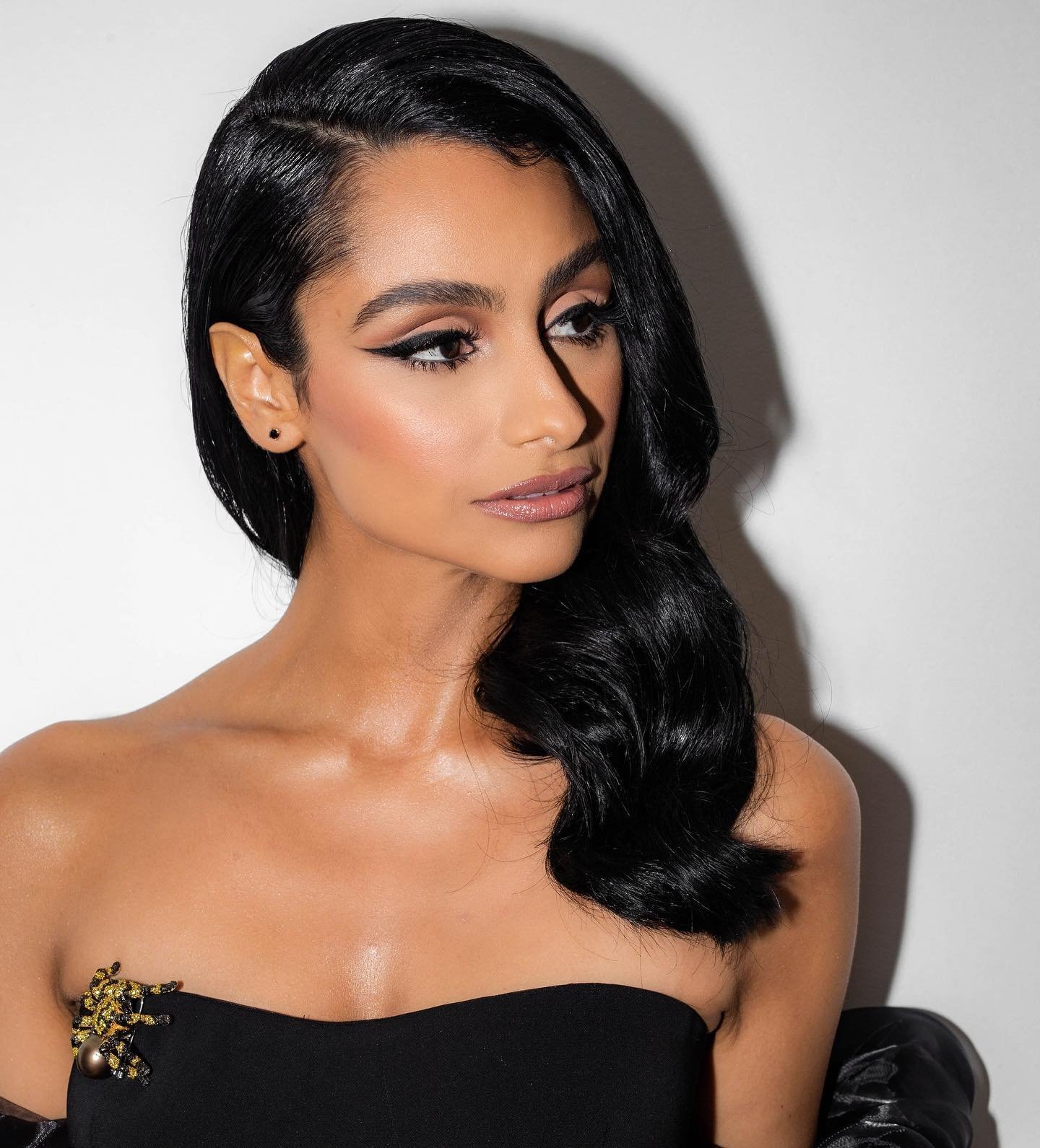 Glamorous headshot of a beautiful woman with long, dark hair and elegant makeup posing against a white background in a strapless black dress.