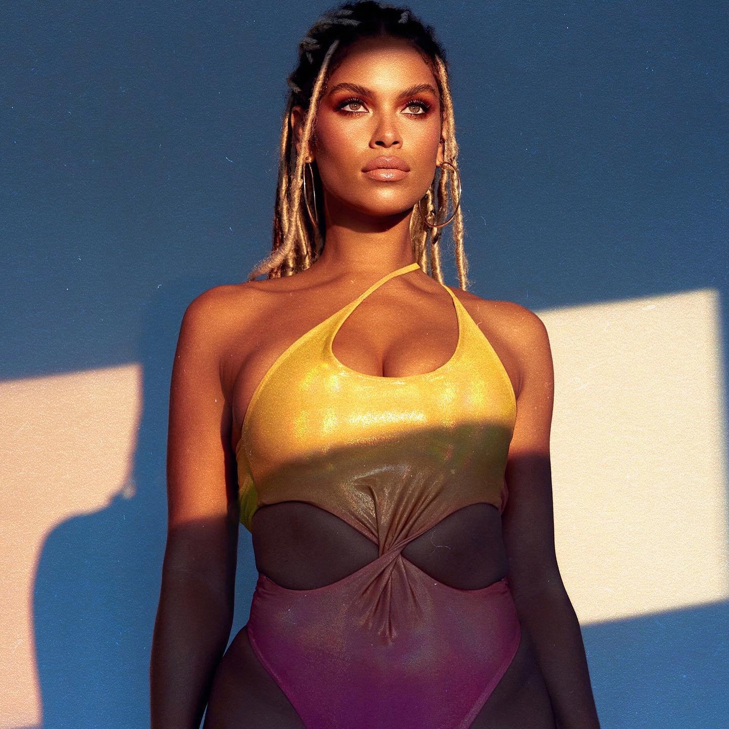 Adult female wearing a vibrant, multicolored swimsuit poses in soft light against a light blue background, creating a summery, fashion-forward image.