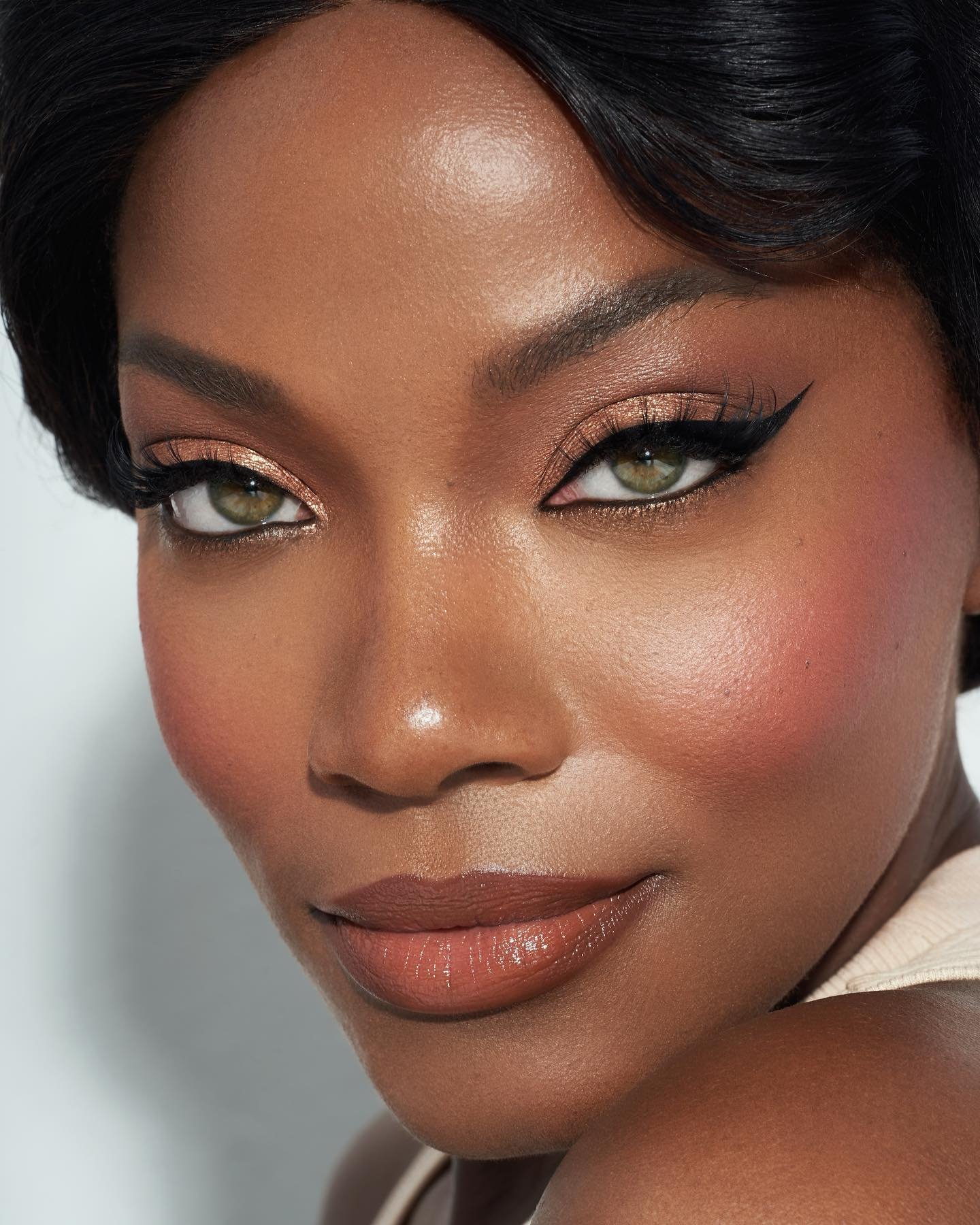 Close-up portrait of a Black woman with green eyes, wearing elegant makeup, showcasing beauty and makeup artistry against a neutral backdrop.
