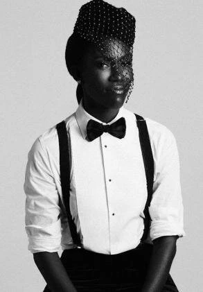 Black and white portrait of an African American woman wearing a formal shirt, bow tie, and headpiece with netting in a minimalist style.