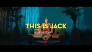 Man in a tan suit sitting on a wooden bench against a teal water backdrop with large yellow text reading THIS IS JACK