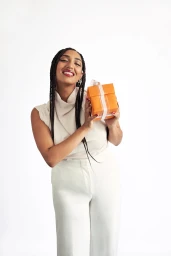 Smiling woman with braided hair holding a small orange gift box against a white background