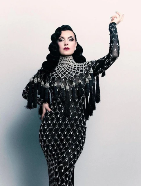 Elegant adult female wearing a floor-length formal gown with black beaded details, dark lipstick, and vintage-style hair, posing in a studio.