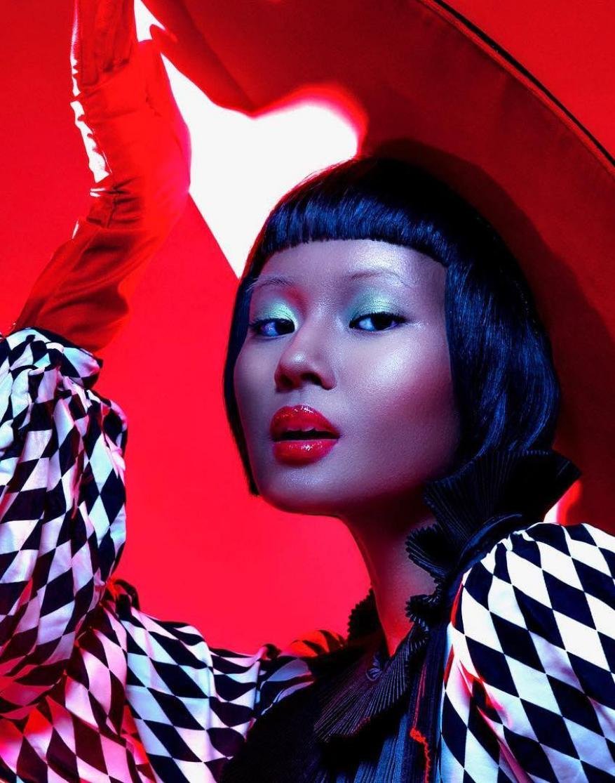 Portrait of a young Asian woman with black hair, glossy red lips, green eyeshadow, and dramatic black and white diamond patterned clothing.