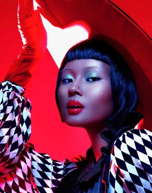 Portrait of a young Asian woman with black hair, glossy red lips, green eyeshadow, and dramatic black and white diamond patterned clothing.