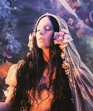 Dreamy portrait of a woman with closed eyes and long, dark wavy hair, adorned with flowers and a sheer head covering, floral background.