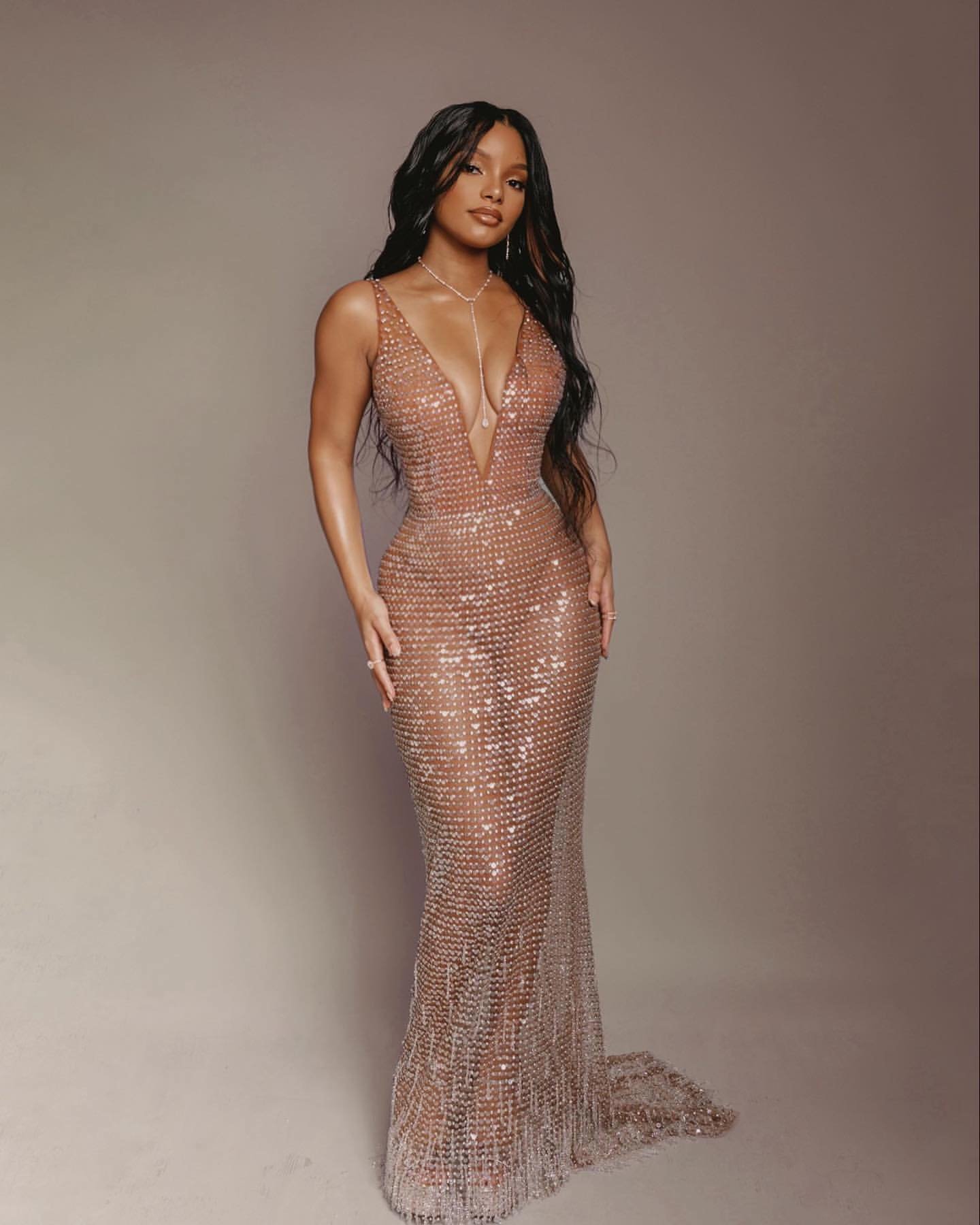 Elegant adult woman in a floor-length, champagne-colored gown with crystal embellishments, posing in a studio with soft lighting.