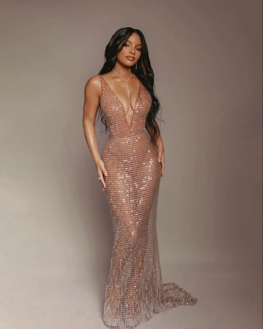 Elegant adult woman in a floor-length, champagne-colored gown with crystal embellishments, posing in a studio with soft lighting.