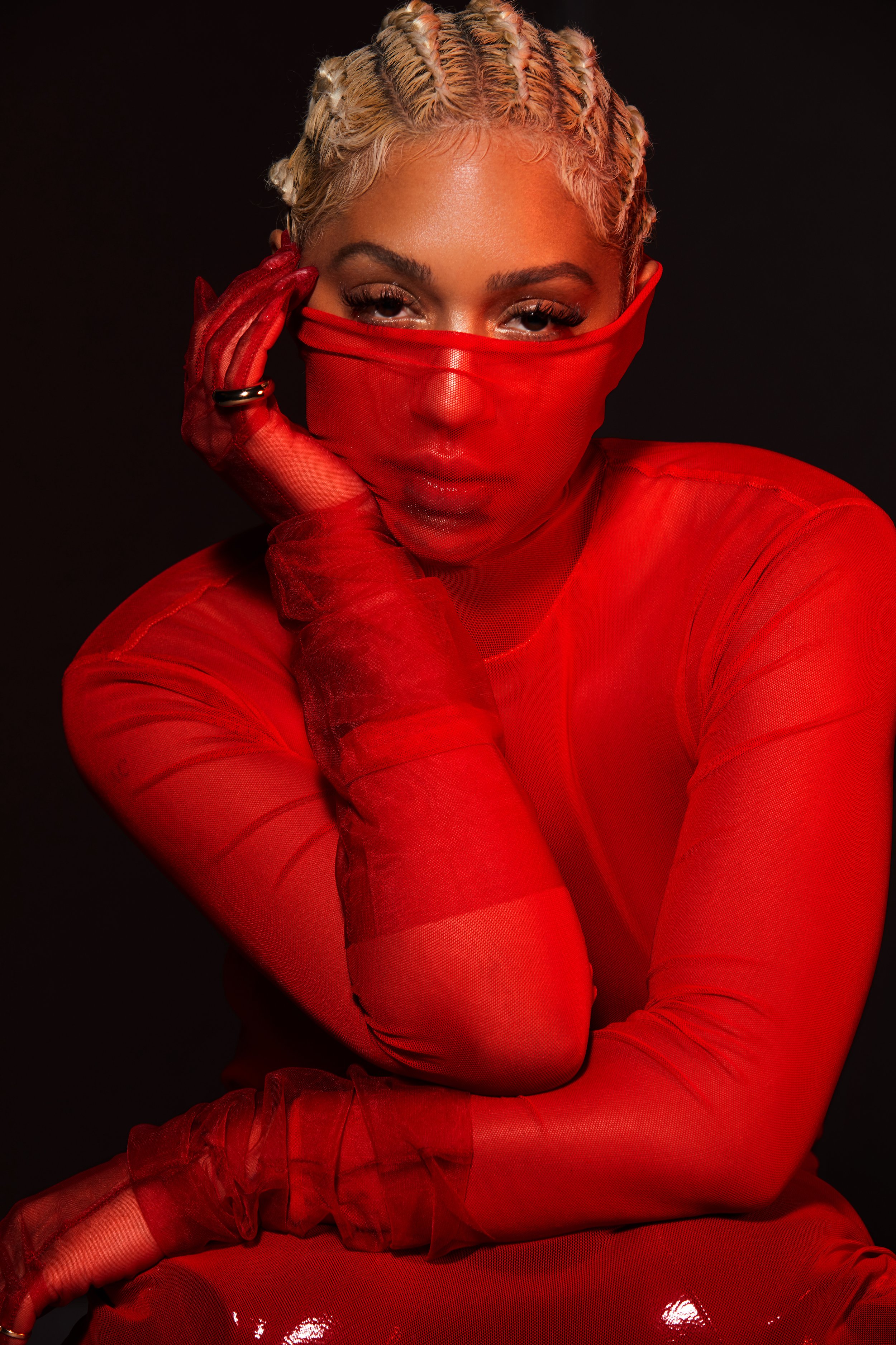 Stylish woman in red mesh top with blonde finger-wave hair posing against a dark background in a beauty or fashion context.