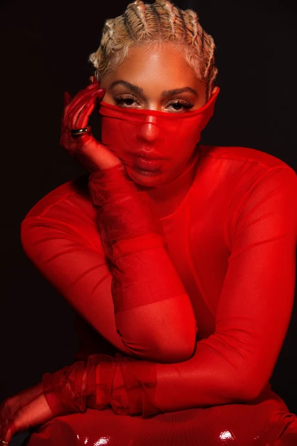 Stylish woman in red mesh top with blonde finger-wave hair posing against a dark background in a beauty or fashion context.