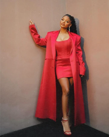Halle Bailey in a red coat and matching mini dress posing against a neutral wall, styled by Nichole Goodman.