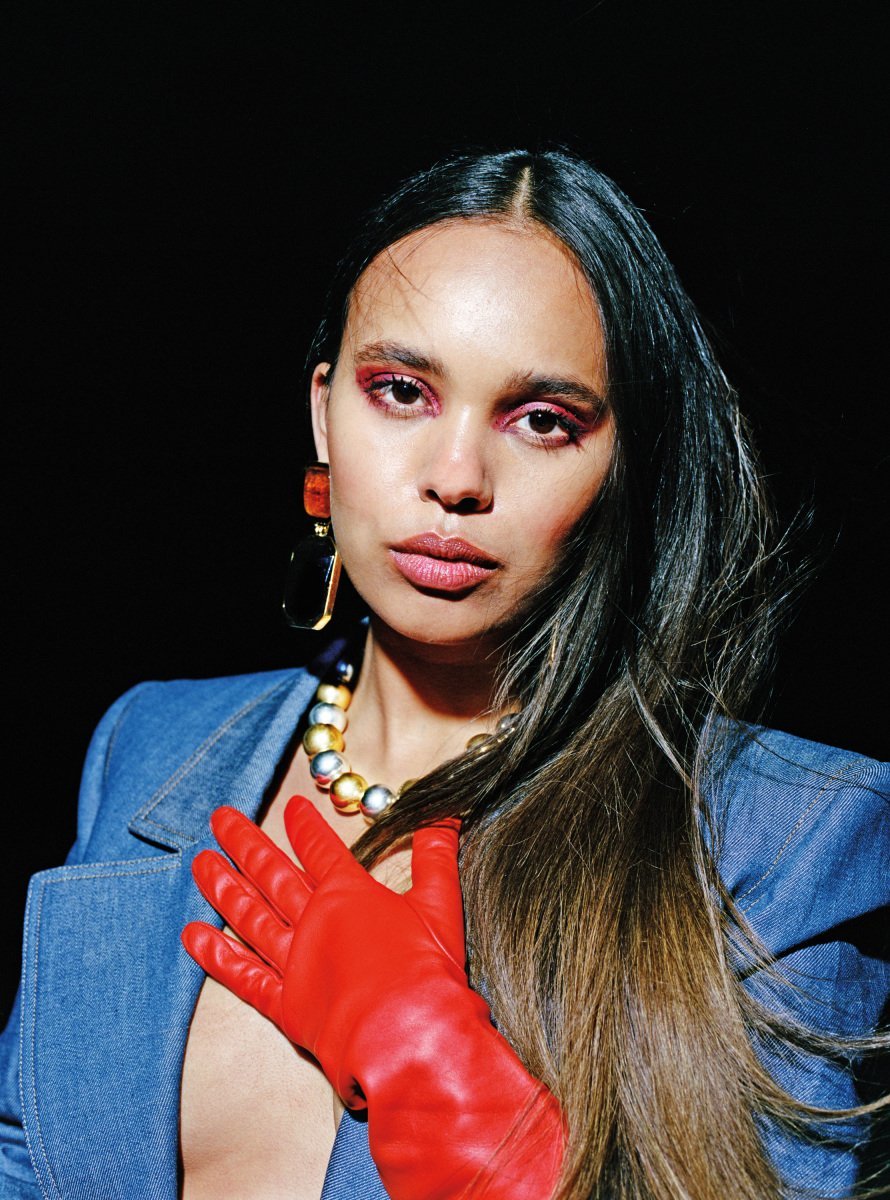 Close-up portrait of a woman wearing a denim jacket, statement jewelry and red glove against a dark background.