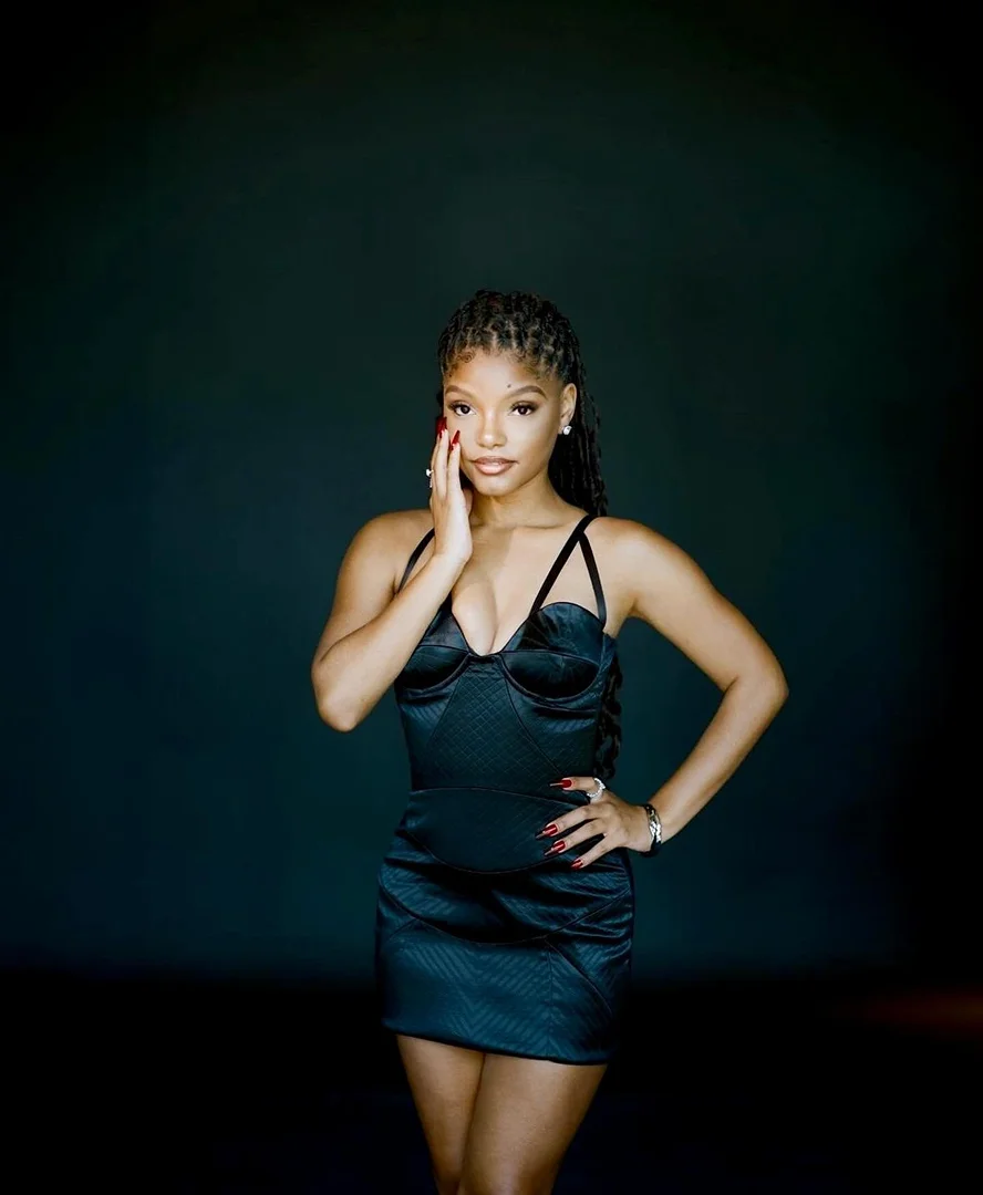 Portrait of Halle Bailey wearing a black satin mini dress with thin straps, styled by Nichole Goodman.