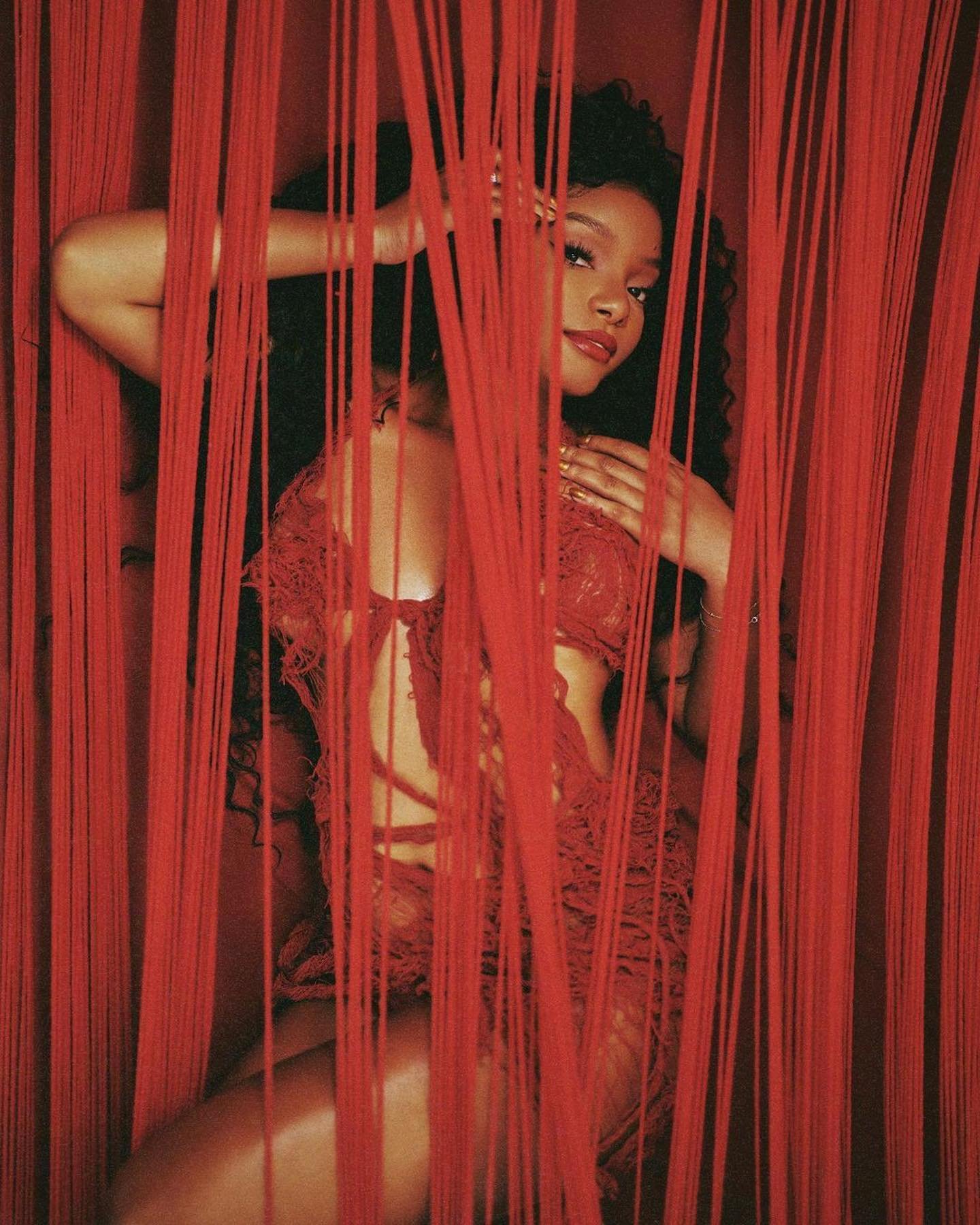 Elegant portrait of a young Black woman posing amid red string curtains, wearing red lace lingerie, with soft lighting and romantic appeal.