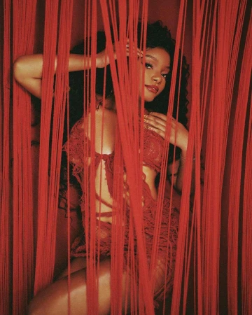 Elegant portrait of a young Black woman posing amid red string curtains, wearing red lace lingerie, with soft lighting and romantic appeal.