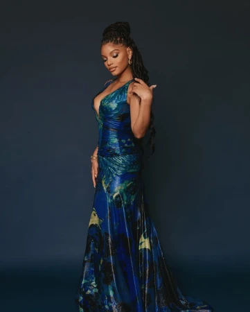 Halle Bailey wearing a long blue patterned evening gown with a plunging neckline against a dark studio background