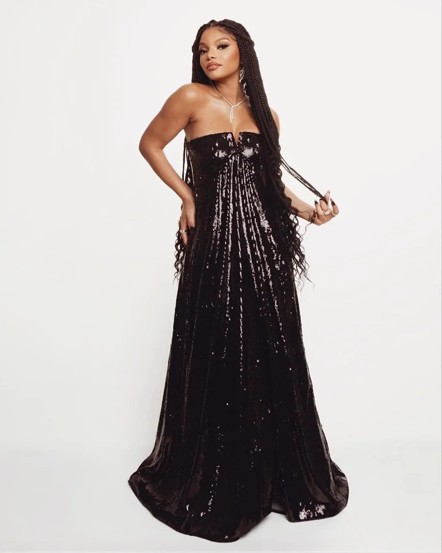 Portrait of a Black woman in a strapless black gown with sequin detail and long braided hair, posing against a white backdrop in studio.