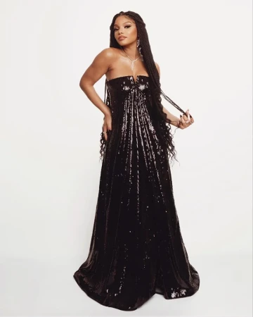 Portrait of a Black woman in a strapless black gown with sequin detail and long braided hair, posing against a white backdrop in studio.