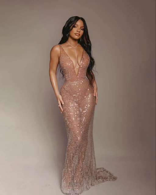 Elegant woman in a shimmering, floor-length gown with a plunging neckline, posing in a studio against a neutral background.