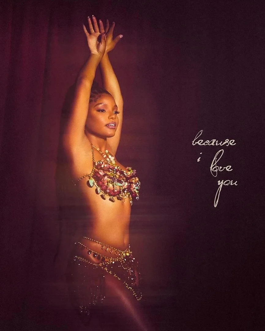 Portrait of a woman with her hands raised and wearing a jeweled bra top, set against a dark background with script overlay.