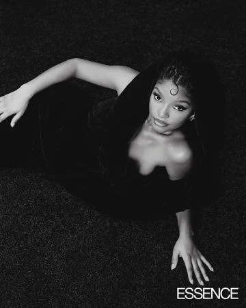 Black and white portrait of Halle Bailey in a black dress lying on a textured surface, styled by Nichole Goodman.