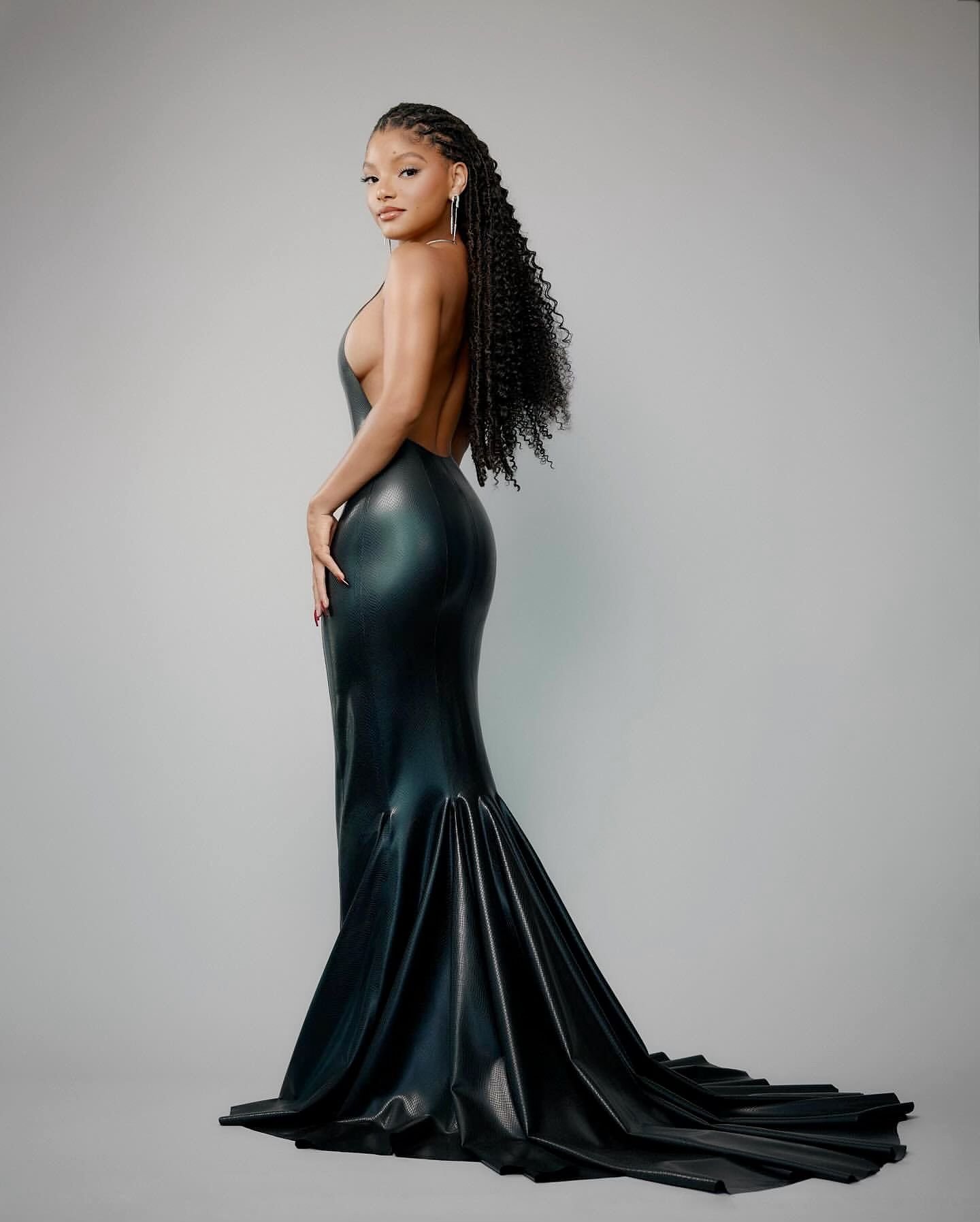 A stylish African-American woman poses in a sleek black dress against a neutral backdrop, showcasing her elegant hairstyle and fashion.