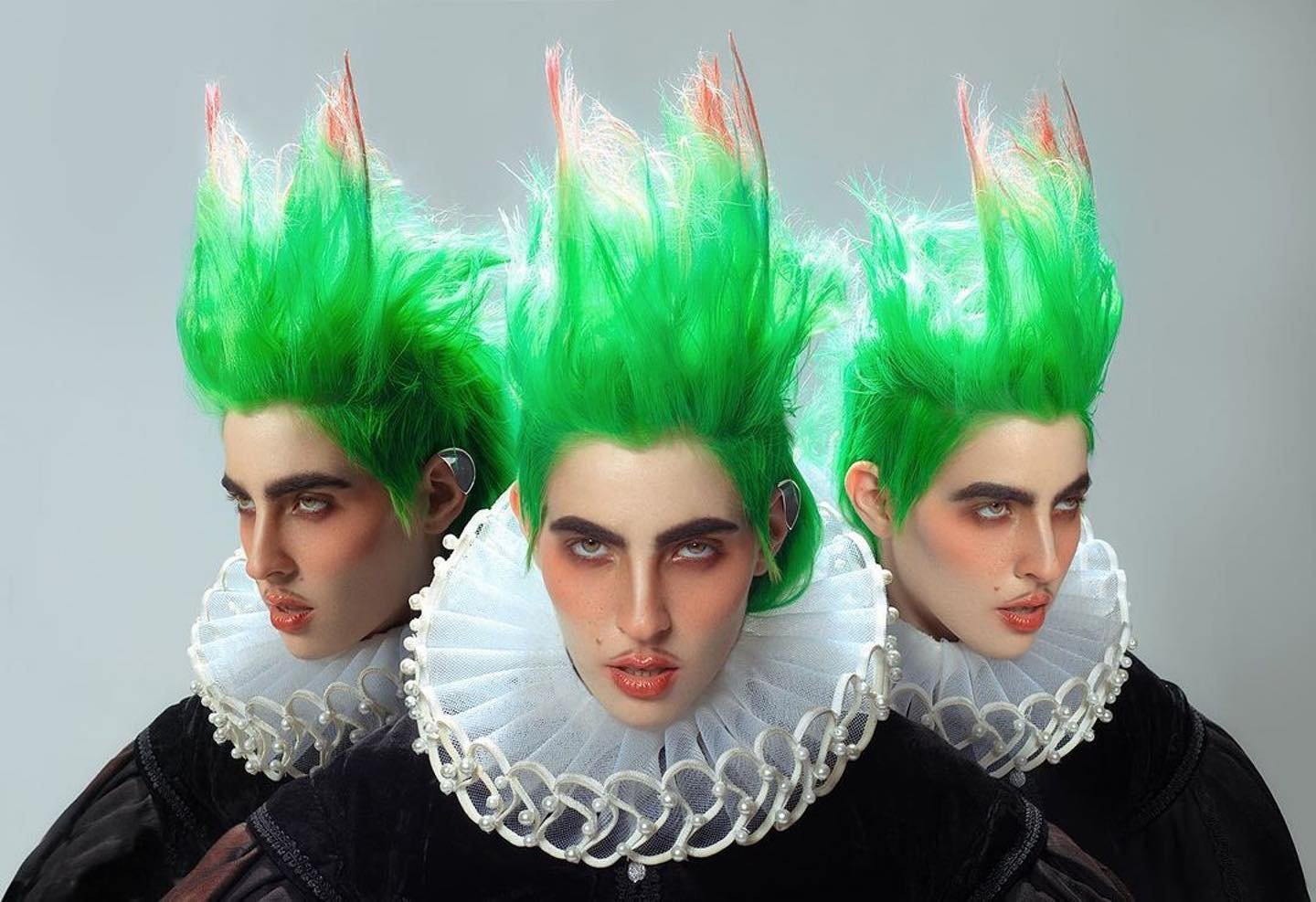 Three models with stylized bright green hair and Elizabethan ruffs pose in front of a neutral background, showcasing high-fashion artistry.