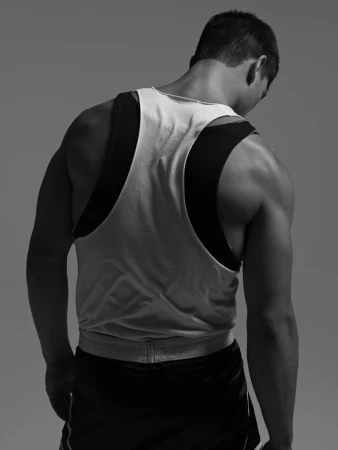 Monochrome, back view of an athletic man wearing a tank top and shorts. He is standing against a plain grey background.