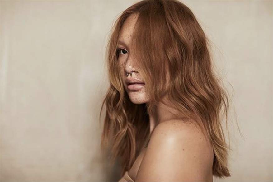 Portrait of a model with long ginger hair, freckles, and septum ring styled by Nicolas Bru against a neutral background