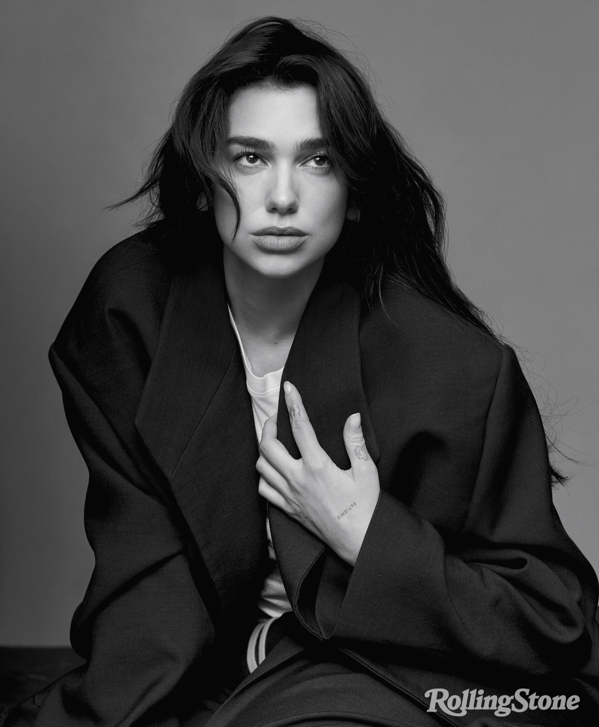 Black and white portrait of Dua Lipa wearing an oversized dark blazer, styled by Nicolas Bru.