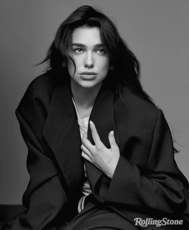 Black and white portrait of Dua Lipa wearing an oversized dark blazer, styled by Nicolas Bru.