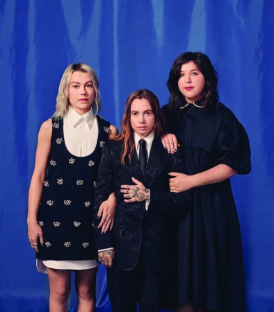 Three musicians posing together against a bright blue draped fabric backdrop with styled black and white attire.