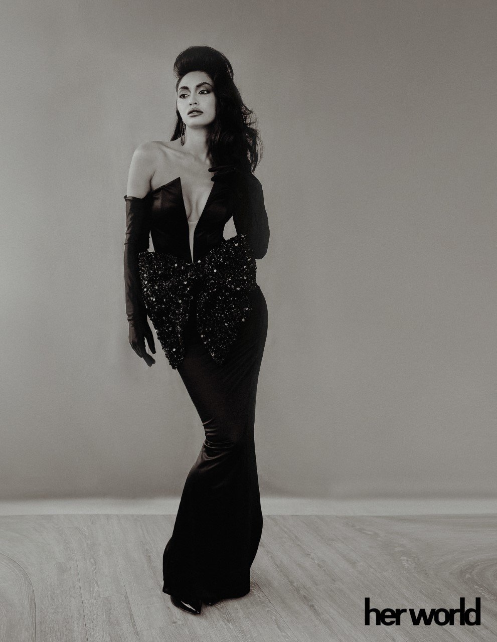 Black and white portrait of a woman in a full-length gown with gloves and sequin detail on a light grey background.