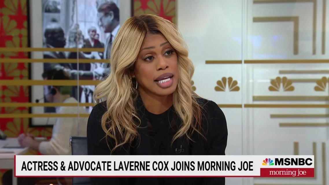 Laverne Cox, actress and advocate, sits on 'Morning Joe' show set with a black top, blond wavy hair, and gold hoop earrings.