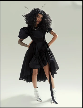 Woman in a black dress with puffed sleeves and silver boots standing against a neutral studio backdrop