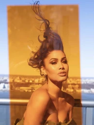 Portrait of a woman with styled hair against an orange tinted glass panel and an urban rooftop view in New York