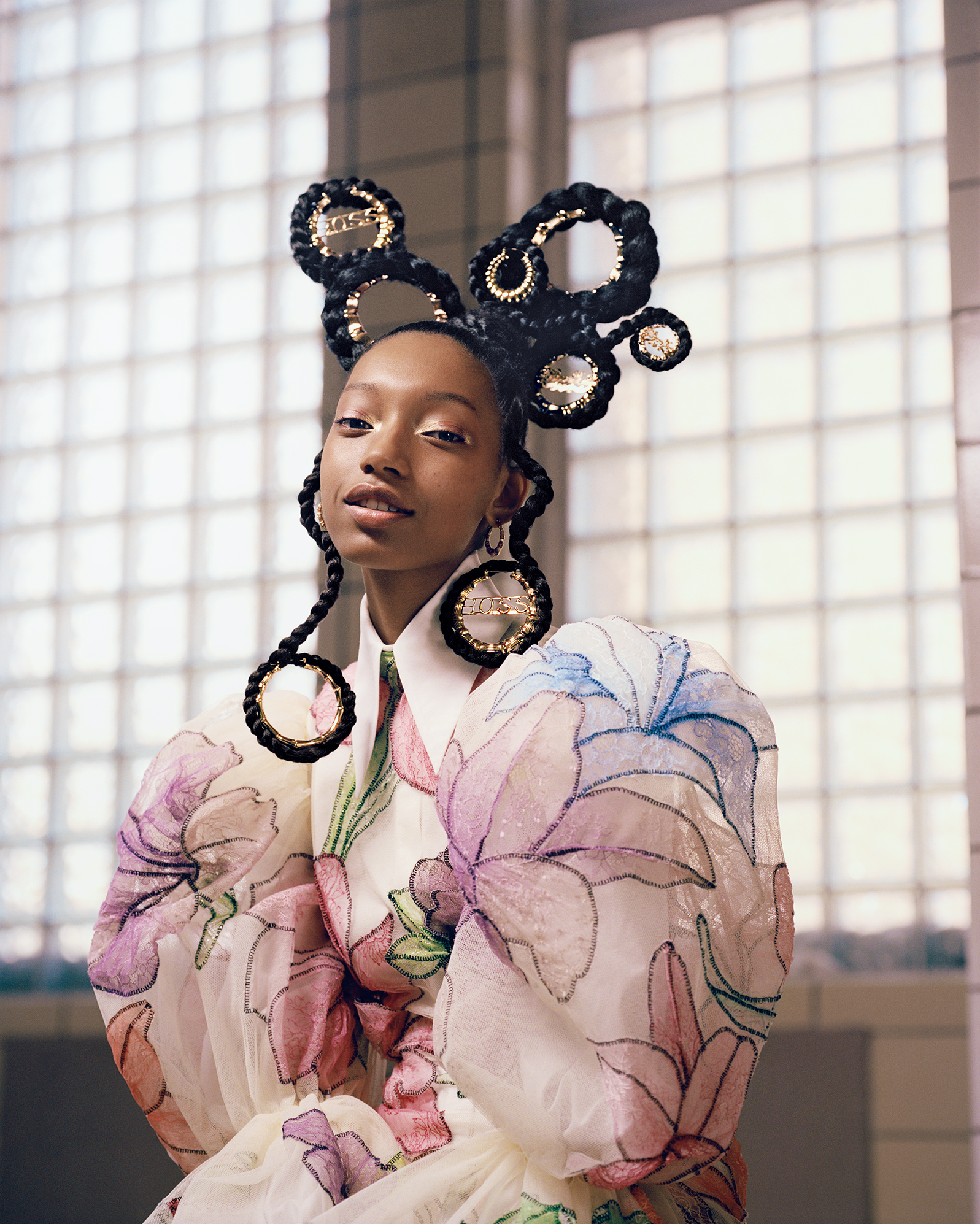 Portrait of African American woman with braided updo and large circular earrings, wearing a floral print dress, indoors.