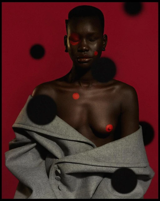 Striking portrait of a Black woman with closed eyes, artistic red dots, wearing a gray coat against a red backdrop.