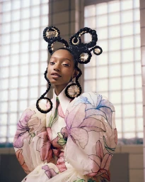 Model with elaborate braided updo and floral puffed-sleeve dress against a tiled window background styled by Nikki Nelms