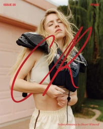 Sydney Sweeney wearing football shoulder pads and white shorts outdoors with red handwritten graphic overlay.